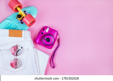 Summer fashion flatlay and white denim jeans  turquoise penny skateboard  purple instant camera   round gradient sunglasses isolated pink background 