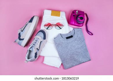 Summer fashion flatlay and white denim jeans  grey shiny t  shirt  blue sneakers  purple instant camera   round gradient sunglasses isolated pink background 