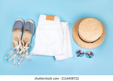 Summer fashion flatlay with white denim jeans, striped espadrilles sandals, straw boater hat and tortoiseshell sunglasses isolated on blue background.