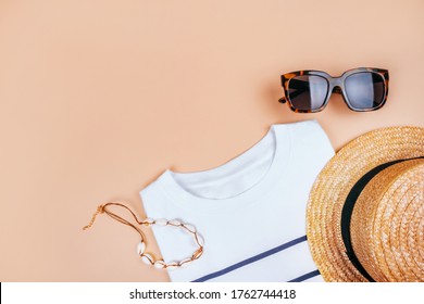 Summer Fashion Flatlay With White Striped T-shirt, Straw Boater Hat, Summer Shell Necklace And Tortoiseshell Sunglasses Isolated On Beige Background.