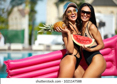 Summer Fashion. Girls In Swimsuits Having Fun Near Pool On Vacation. Sexy Female Models In Trendy Sunglasses And Fashionable Swimwear With Tanned Bodies, Air Mattress And Fruits. High Quality Image.