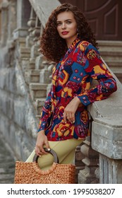 Summer Fashion Portrait Of Elegant Woman Wearing Trendy Colorful Printed Shirt, Holding Wicker Straw Bag, Posing In City