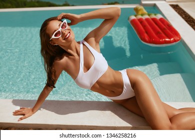 Summer Fashion. Woman In Swimsuit And Sunglasses Sunbathing Near Swimming Pool With Watermelon Float. Girl Model In Swimwear Enjoying Vacation Near Infinity Pool 