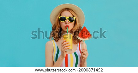 Summer fashionable colorful portrait of stylish young woman drinking juice with lollipop or ice cream shaped slice of watermelon wearing a straw hat on blue background