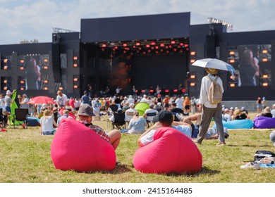 Summer festival vibes with enthusiastic crowd relaxing and watching a live concert outdoors under clear skies. - Powered by Shutterstock