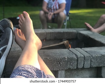 Summer Firepit Scene With Barefoot Feet Up In Lawn Chairs On Green Grass In Backyard