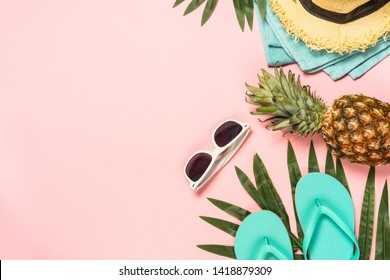 Summer flat lay background. Beach accessories with palm leaves, flip flops, pineapple, sunglasses, hat and starfish on pink background. Top view with copy space.