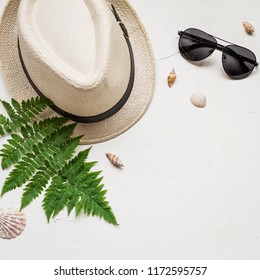 Summer Flat Lay With A Hat And A Green Fern, A Red Sea Star, Seashells And Glasses On White Concrete Background.