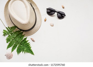 Summer Flat Lay With A Hat And A Green Fern, A Red Sea Star, Seashells And Glasses On White Concrete Background.