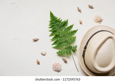 Summer Flat Lay With A Hat And A Green Fern, A Red Sea Star, Seashells And Glasses On White Concrete Background.