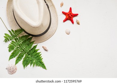 Summer Flat Lay With A Hat And A Green Fern, A Red Sea Star, Seashells And Glasses On White Concrete Background.