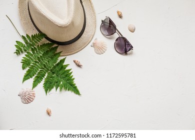 Summer Flat Lay With A Hat And A Green Fern, A Red Sea Star, Seashells And Glasses On White Concrete Background.