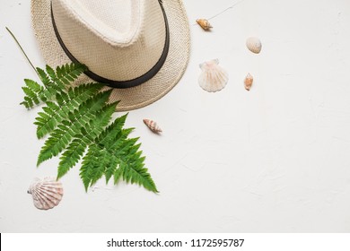 Summer Flat Lay With A Hat And A Green Fern, A Red Sea Star, Seashells And Glasses On White Concrete Background.