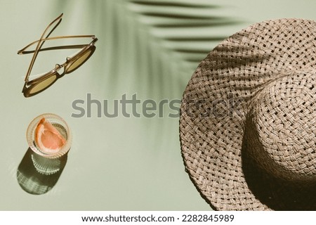 Summer flat lay with straw hat, sunglasses and glass of water with grapefruit slices on green background with palm leaf shadow, sun and sunlight. Vacation, holiday, summer creative minimal concept