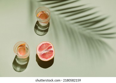 Summer Flat Lay With Two Glasses Of Refreshment Drinks And Grapefruit Slices On Green Background With Palm Leaf Shadow Sun And Sunlight. Vacation, Holiday, Mocktail, Creative Minimal Concept