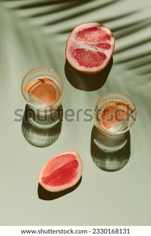 Summer flat lay with two glasses of refreshment drinks and grapefruit slices on green background with palm leaf shadow sun and sunlight. Vacation, holiday, mocktail, creative minimal concept