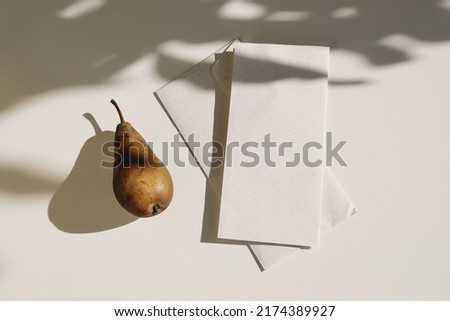 Summer food still life. Autumn weddding greeting card. Folded menu card, envelope mock up from textured craft paper. Pear fruit, long harsh shadows overlay. Beige table background in sunlight. Flatlay