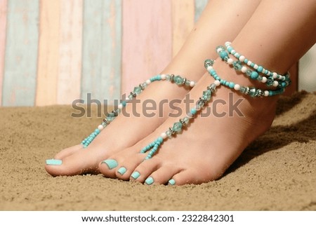 Summer foot jewelry in boho style. Close-up on the feet of a girl sitting on the beach, wearing barefoot sandals and anklet beaded jewelry. Beach fashion trends.