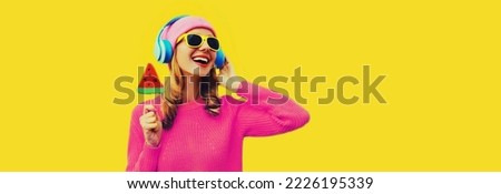 Summer fresh colorful portrait of happy laughing young woman in headphones listening to music with fruit juicy lollipop or ice cream shaped slice of watermelon on yellow background
