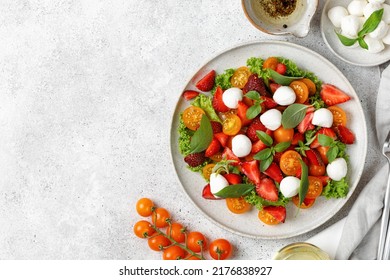 Summer fresh diet salad with cherry tomatoes, mozzarella cheese, strawberry, basil and olive oil on grey background. Healthy lunch. Top view, copy space. - Powered by Shutterstock