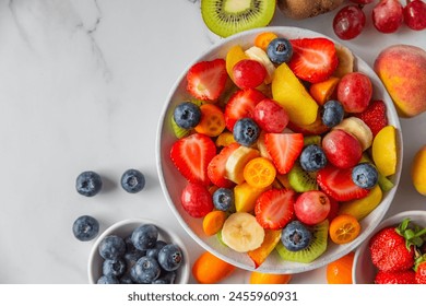 Summer fresh fruit salad in a bowl on white marble background. Top view with copy space. Healthy food for breakfast. Mixed strawberries, grapes, banana, kiwi, blueberries, peach, citrus for diet lunch - Powered by Shutterstock