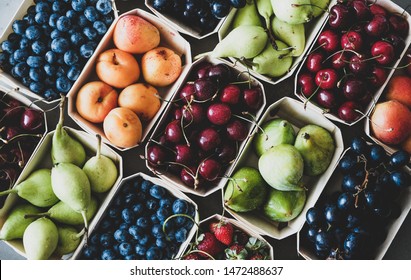 Summer fruit and berry variety. Flat-lay of ripe strawberries, cherries, grapes, blueberries, pears, apricots, figs in wooden eco-friendly boxes over grey background, top view. Local farmers produce
