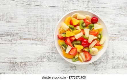 Summer Fruit Salad In A Plate Of Chopped Strawberries, Kiwi, Banana, Orange And Cherry On White Wooden Background. Top View With Copy Space. Healthy Organic Food.