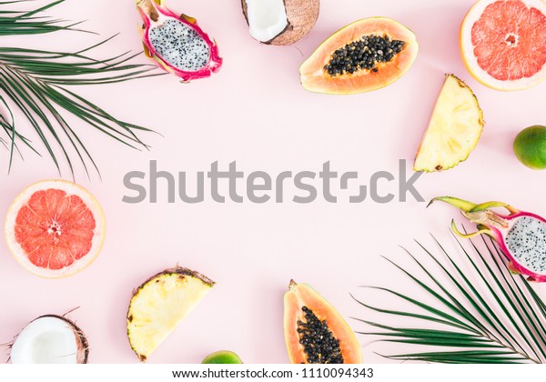 Summer fruits. Tropical palm leaves, pineapple,\
coconut, papaya, dragon fruit, orange on pastel pink background.\
Flat lay, top view, copy\
space