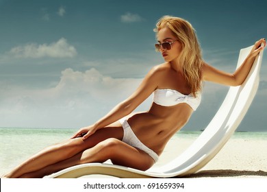 Summer girl model with tanned sexy body. Posing in the white chair on the beach of the tropical island