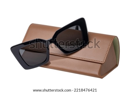 Summer glasses fashion. Female elegant trendy luxury black sun glasses resting on a brown leather case isolated on a white background. Clipping path. Macro.