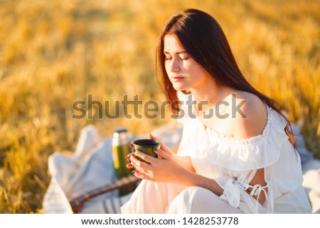 Summer is a great dream time. Back view of young girl with pink hair wearing black, holding thermo bottle in field of rapeseed.