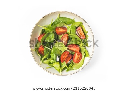 Summer green salad in white bowl plate isolated on white backgorund. Healty salat from tomato, spinach, onion and green leaves with oil for dinner or lunch. Vegetarian food concept. Top view