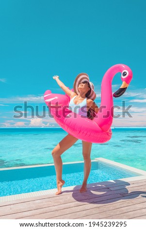 Summer happy woman relaxing sunbathing at luxury infinity pool swimming with pink funny flamingo float. Joyful tanning girl in swimsuit on hotel Caribbean vacation.