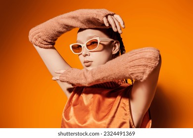 Summer haute couture collection. Fashion model girl posing in stylish glasses and an orange top on an orange studio background. Fashion and style for sunglasses.