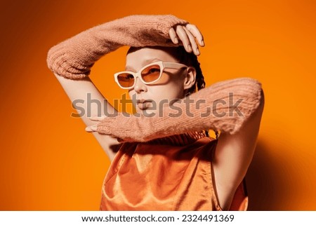 Summer haute couture collection. Fashion model girl posing in stylish glasses and an orange top on an orange studio background. Fashion and style for sunglasses.