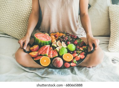 Summer Healthy Raw Vegan Clean Eating Breakfast In Bed Concept. Young Girl Wearing Pastel Colored Home Clothes Sitting And Holding Tray Full Of Fresh Seasonal Fruit