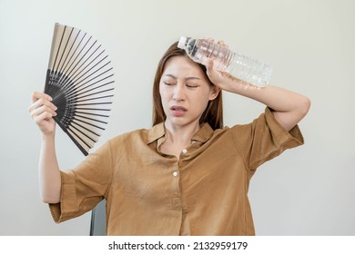 Summer heat stroke, hot weather, tired asian young woman sweaty and thirsty, refreshing with hand in blowing, wave fan to ventilation, holding cold water bottle tap her body when temperature high.