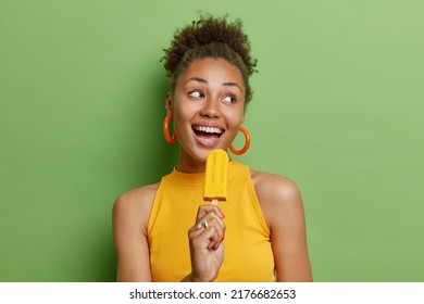 Summer is here. Positive carefree woman holds delicious ice cream as if microphone has sweet tooth looks gladfully away dressed in t shirt poses against bright green background. Delicacy concept - Powered by Shutterstock