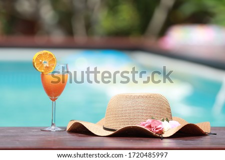 Summer holiday  by the pool. This picture has a relaxed vibe featuring a drink with fresh oranges and a woman's sunbathing hat. The background consists  of a blurred out pool,a pink floaty and some gr Imagine de stoc © 