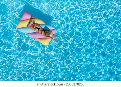 Summer Holiday Concept With A Beautiful, Blonde Woman Relaxing On A Colorful Float Over Blue, Sparkling Pool Water