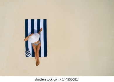 Summer Holiday Fashion Concept - Tanning Girl Wearing Sun Hat At The Beach On A White Sand Shot From Above.Top View From Drone. Aerial View Of Slim Woman Sunbathing Lying On A Beach In Maldives.