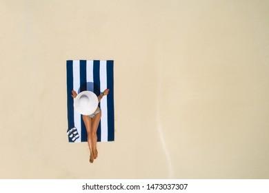 Summer Holiday Fashion Concept - Tanning Girl Wearing Sun Hat At The Beach On A White Sand Shot From Above.Top View From Drone. Aerial View Of Slim Woman Sunbathing Lying On A Beach In Maldives.