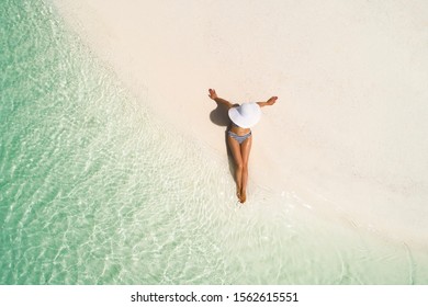 Summer holiday fashion concept - tanning girl wearing sun hat at the beach on a white sand shot from above.Top view from drone. Aerial view of slim woman sunbathing lying on a beach in Maldives. - Powered by Shutterstock