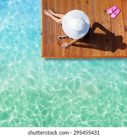 Summer Holiday Fashion Concept - Tanning Woman Wearing Sun Hat At The Pool On A Wooden Pier Shot From Above