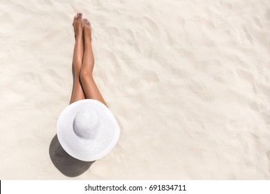 Summer Holiday Fashion Concept - Tanning Woman Wearing Sun Hat At The Beach On A White Sand Shot From Above