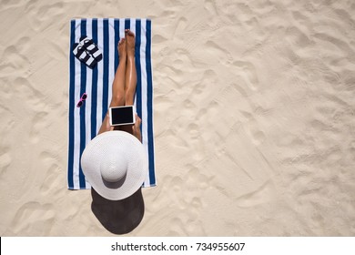 Summer Holiday Fashion Concept - Tanning Woman Wearing Sun Hat At The Beach On A White Sand Shot From Above