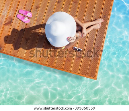 Summer holiday fashion concept - tanning woman wearing sun hat at the pool on a wooden pier shot from above