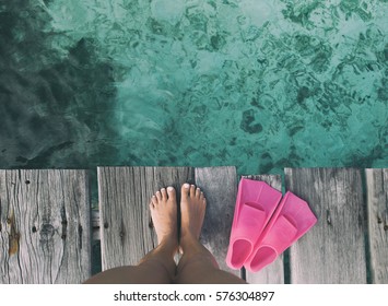 Summer holiday fashion selfie concept - woman feet on a wooden pier at the beach with pink fins flippers