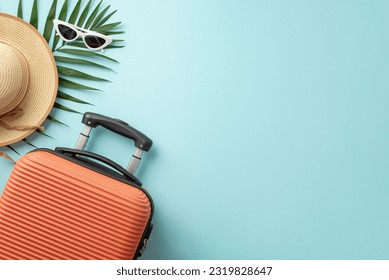 Summer holiday inspiration. Top view of a bright suitcase, beach gear, sunhat, and palm fronds on a pastel blue backdrop, ideal for text or advertising