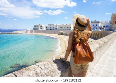 Summer holiday in Italy. Back view of young woman with hat and backpack in Gallipoli village, Salento, Italy.
